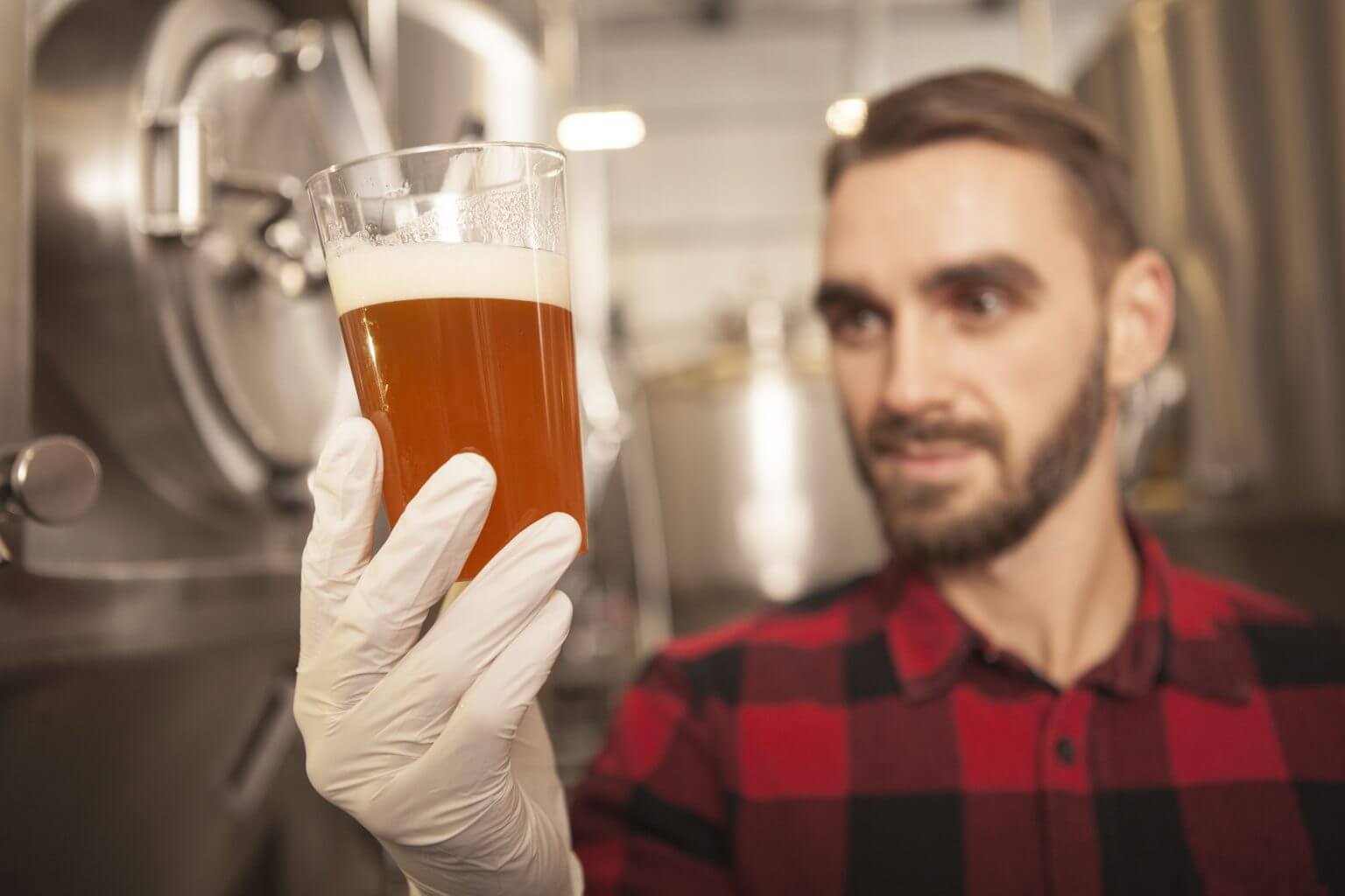 Handsome brewer examining freshly brewed beer at his beer factor